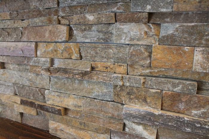 close up of a stacked stone backsplash, made from uneven grey, brown and beige pieces of stone, near a dark wooden surface