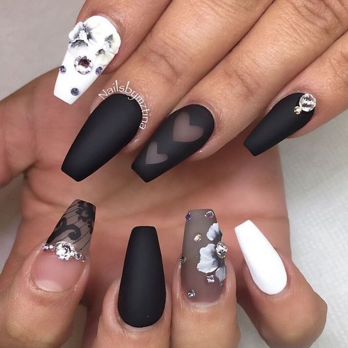 sheer and opaque nail polish, in black and white, on a set of fake nails, decorated with grey flowers and rhinestones