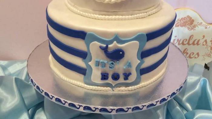 whale shape in dark blue, and the words it's a boy, decorating a white cake, with three dark blue stripes, and two strings of pearls