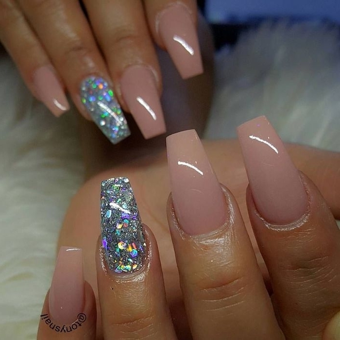 glossy nude pink nails, on two hands with coffin style manicure, both ring finger nails are covered in iridescent glitter flakes