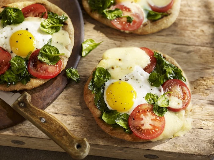massive wooden table, with a cutting board and a knife, and three flatbreads, topped with cheese, tomato slices and basil leaves, and a baked egg, easy breakfast recipes 