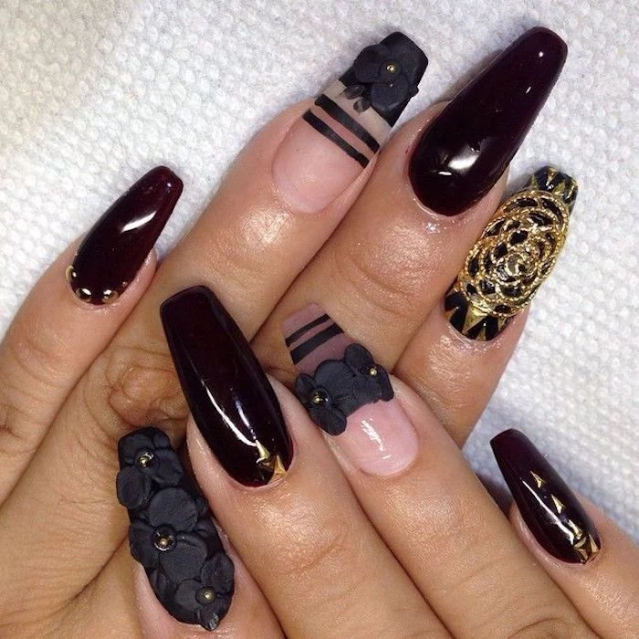 flowers made from black acrylic, decorating a manicure, with clear and very dark cherry red nail polish, coffin nail designs, with black stripes and gold motifs