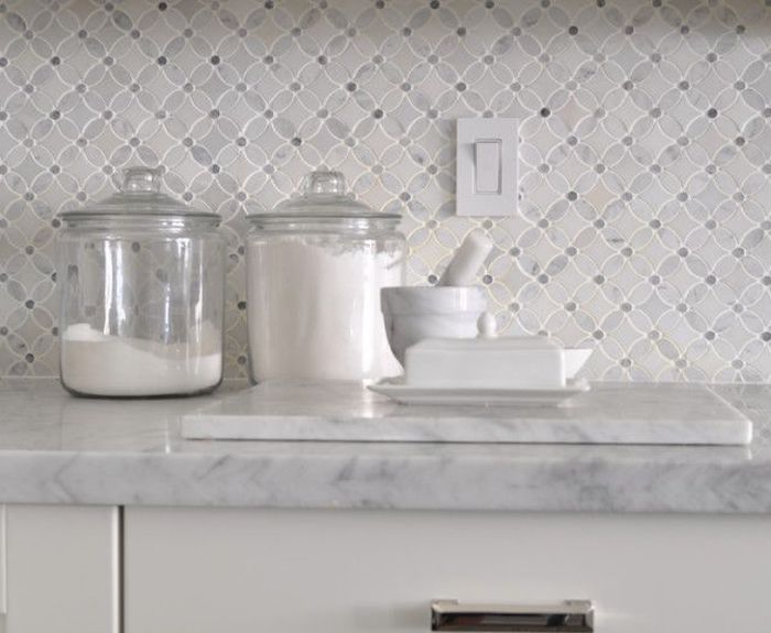 clear glass jars with lids, containing salt of flour, on a light marble counter top, near a small mortar and pestle, white and pale grey arabesque tile backsplash