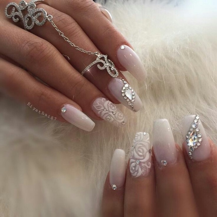 roses painted in white acrylic, on the ring finger nails of two hands, the rest of the nails are white, and decorated with rhinestones