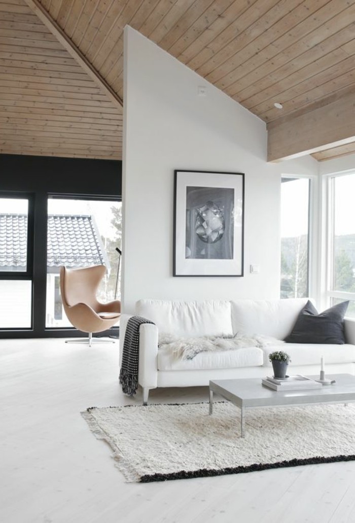 bright space with a wooden vaulted ceiling, large windows and white walls, containing a white sofa, with dark grey cushion and throw, how to decorate a living room