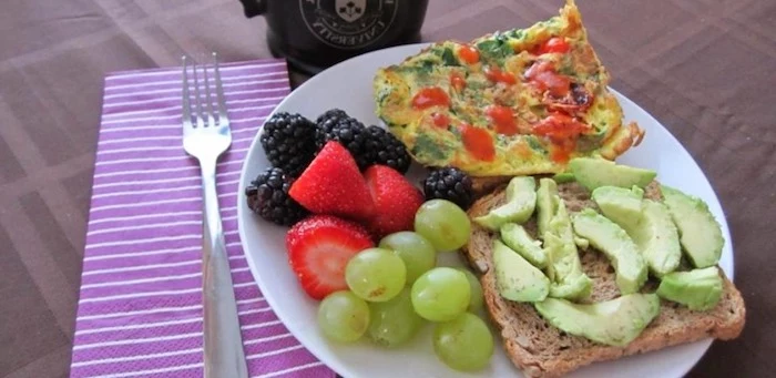 blackberries and strawberries and grapes, near a piece of toast, covered with avocado slices, and a piece of vegetable frittata 
