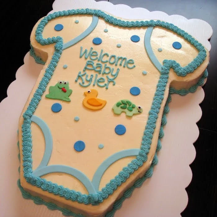 turtle and frog shapes in green, and a duckling shape in yellow, decorating a pale yellow cake, with blue frosting, onesie cake