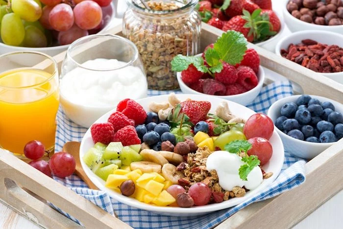 mango and kiwi pieces, banana slices and grapes, and strawberries and raspberries, in a white ceramic plate, with a dollop of yoghurt, and some muesli