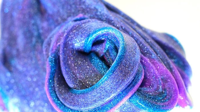 fine powdery glitter, decorating a twisted piece, of galaxy-inspired elmer's glue slime, in violet and purple, with blue streaks