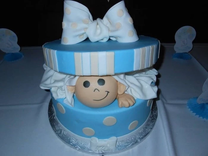 round cake shaped like an open blue present, with cream and white stripes, a big pale blue bow, and a baby peeking from within