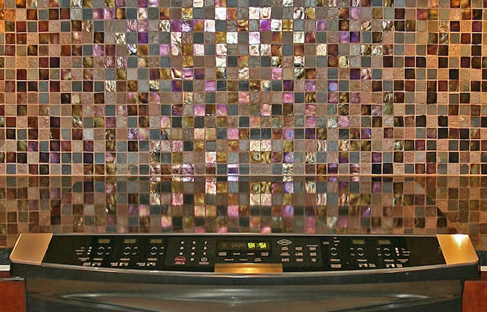 iridescent glittering mosaic tiles, in grey and pink, blue and purple, on a kitchen wall, near a smooth, dark counter top, glass mosaic tile backsplash 