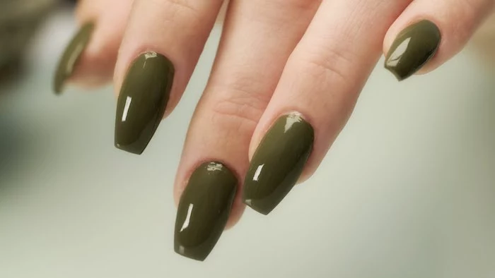 coffin shaped nails, painted in olive green, smooth and glossy nail polish, on the fingers of a hand, seen in close up