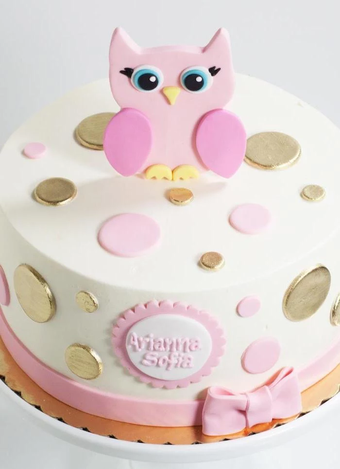 buttons in metallic gold, and pale pink colors, decorating a white cake, topped with a pink owl figurine, owl baby shower cake, the name arianna sofia, written in pink