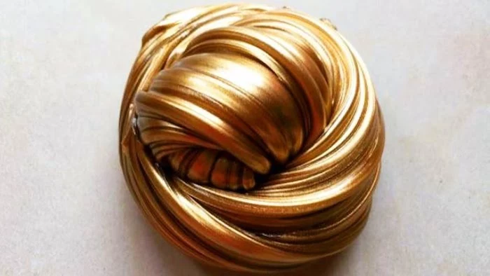 metallic fluffy slime, in a shiny golden color, shaped into a knot-like, twisted round shape, placed on a pale beige surface