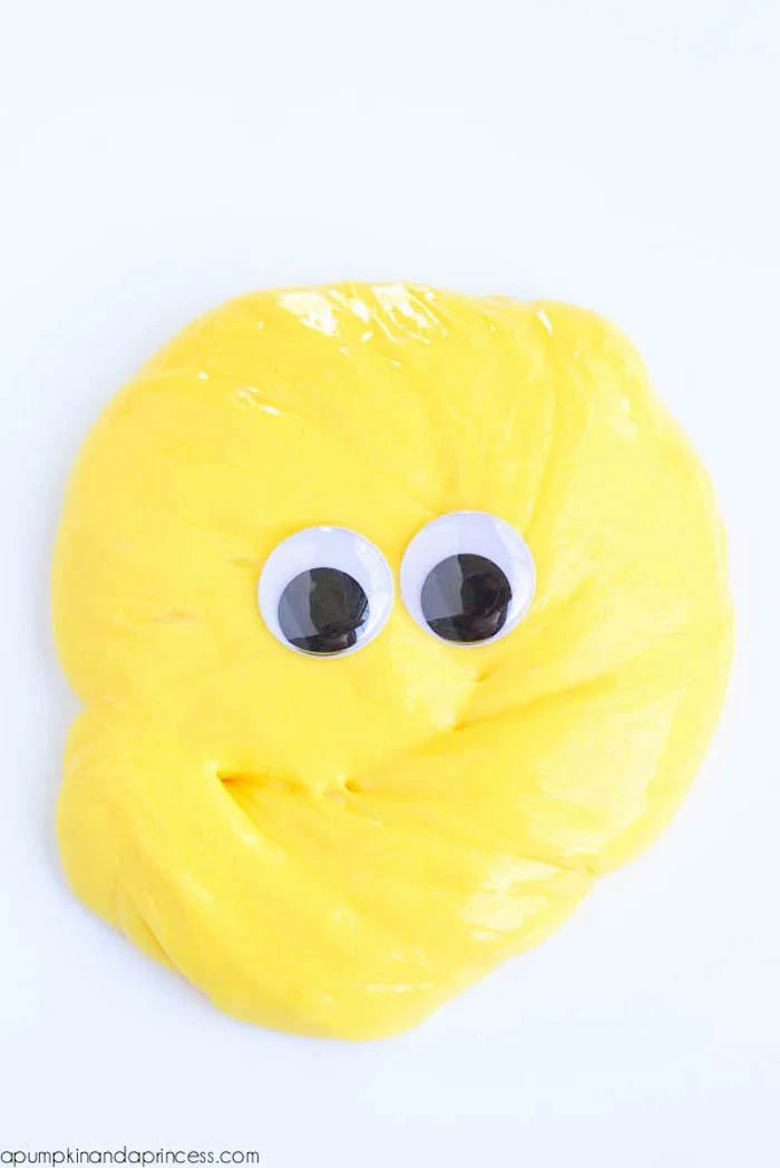 slime recipe without borax, yellow glob of goo, placed on a smooth white surface, and decorated with two googly eye stickers, in black and white