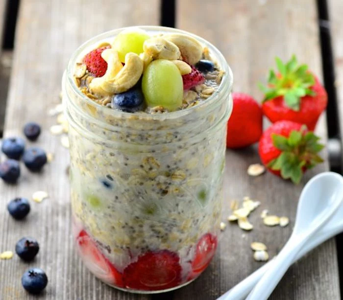 cashew nuts and blueberries, grapes and strawberries, on top of a clear glass jar, containing milk and oats, best breakfast for weight loss, more strawberries and blueberries nearby
