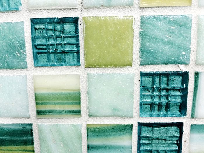 opaque and transparent, pale blue and green square tiles, some with stripes, in a glass mosaic tile backsplash, seen in extreme close up