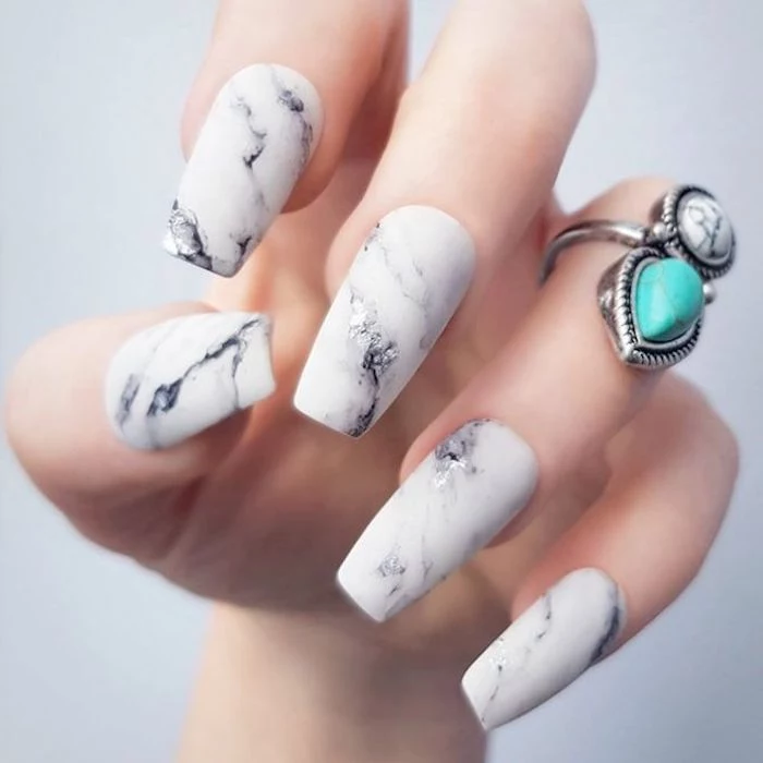 patterned coffin acrylic nails, resembling a marble surface, in white and grey, on a pale hand, with a chunky boho ring
