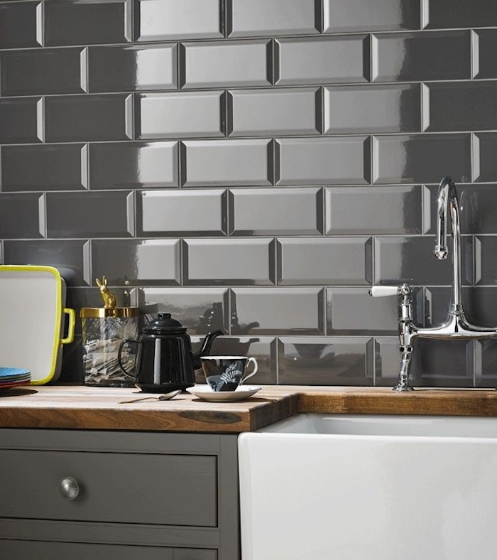 reflective and glossy, grey subway tile back splash, near a wooden counter top, with an inbuilt white sink, and grey cabinets