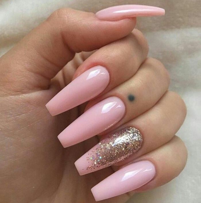 folded fingers with long coffin nails, painted in a pale baby pink hue, the ring finger nail is decorated with iridescent glitter