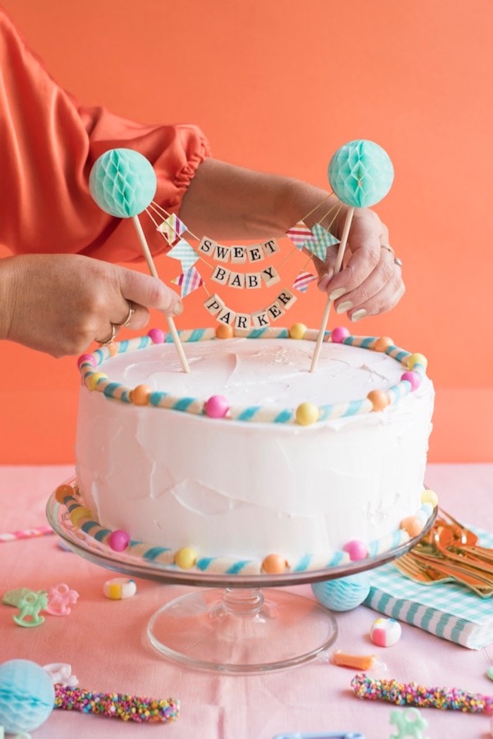 sweet baby parker, written on a cake topper, with two pale turquoise, round paper decorations, placed on a creamy white cake, by two hands