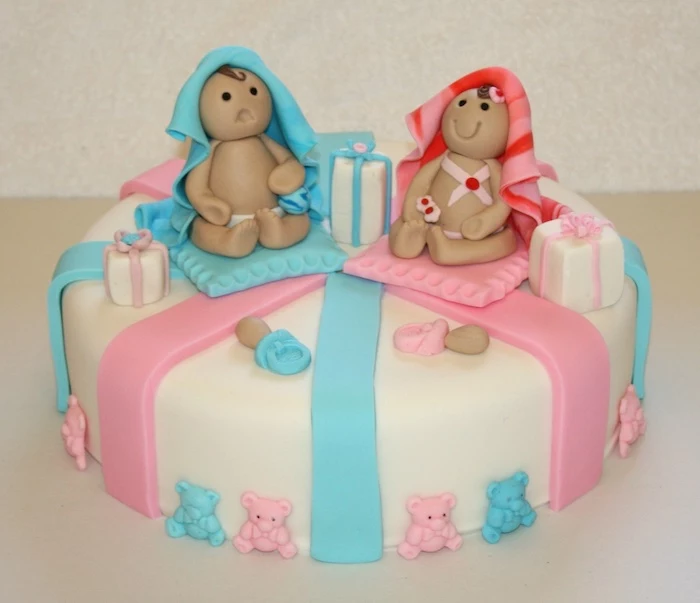 frowning and smiling baby figurines, one covered in a blue blanket, and one in a striped, red and pink blanket, twin baby shower cakes, smooth white cake with fondant decorations