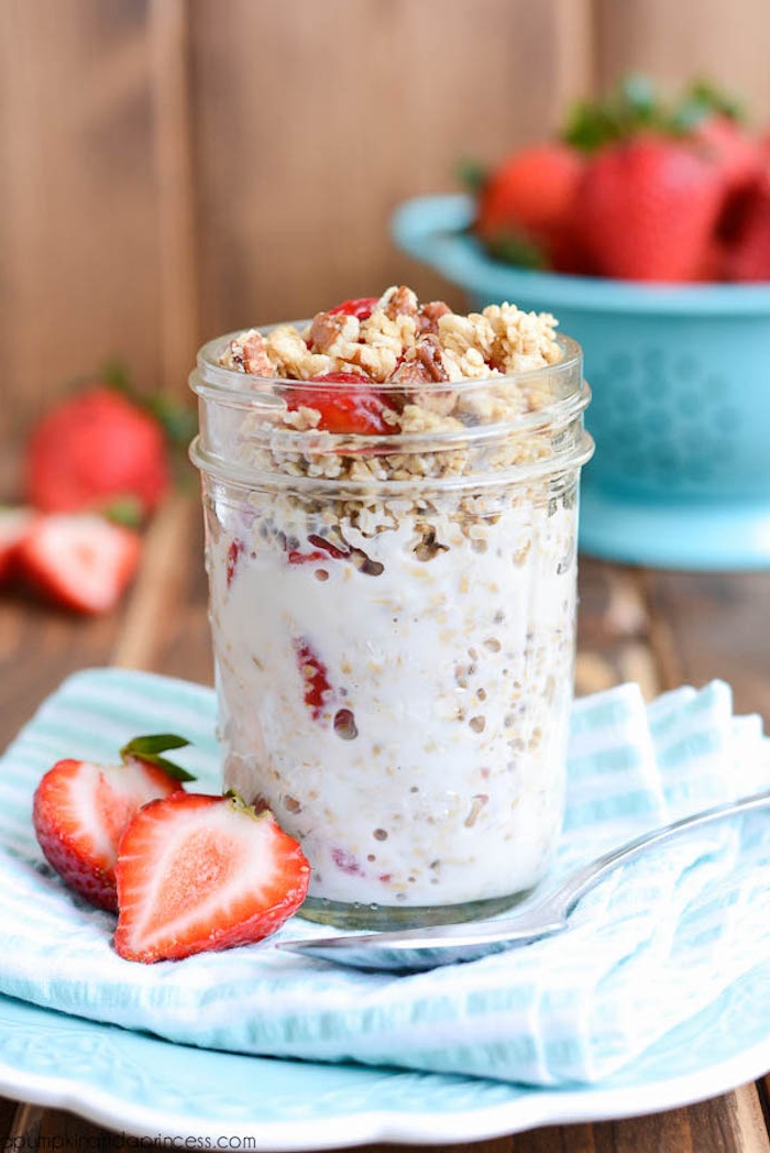 strawberry cut in halves, near a small jar, best breakfast for weight loss, filled with yoghurt and muesli, and topped with crunchy granola, and red fruit