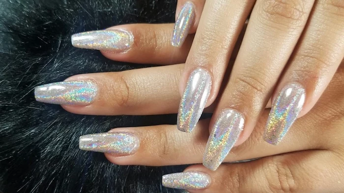 iridescent hologram nails, with soft yellow, orange and pale blue reflections, on two hands, resting on a black, fur-like surface, acrylic nail shapes