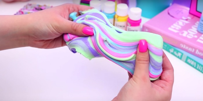 fluffy slime recipe, two hands with hot pink nail polish, kneading a piece of multicolored goo, in pastel colors, minty green and pale purple, pink and blue