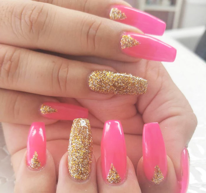 triangles made of gold glitter, decorating the long hot pink squoval nails, of two hands, both ring finger nails are entirely covered in gold glitter