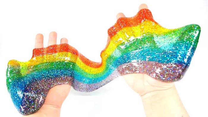 rainbow colored slime without borax, semi-transparent and stretched between two hands, violet and blue, green and red, and yellow on a white background