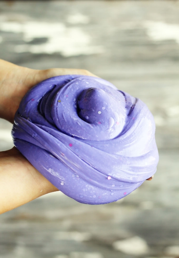 hands holding a large piece of fluffy slime, glossy and smooth, with pink and silver glitter, shaped into a round pile