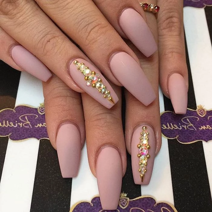 ring finger nails decorated with rhinestones, on two hands with long, nude coffin nails, in a pinky beige shade