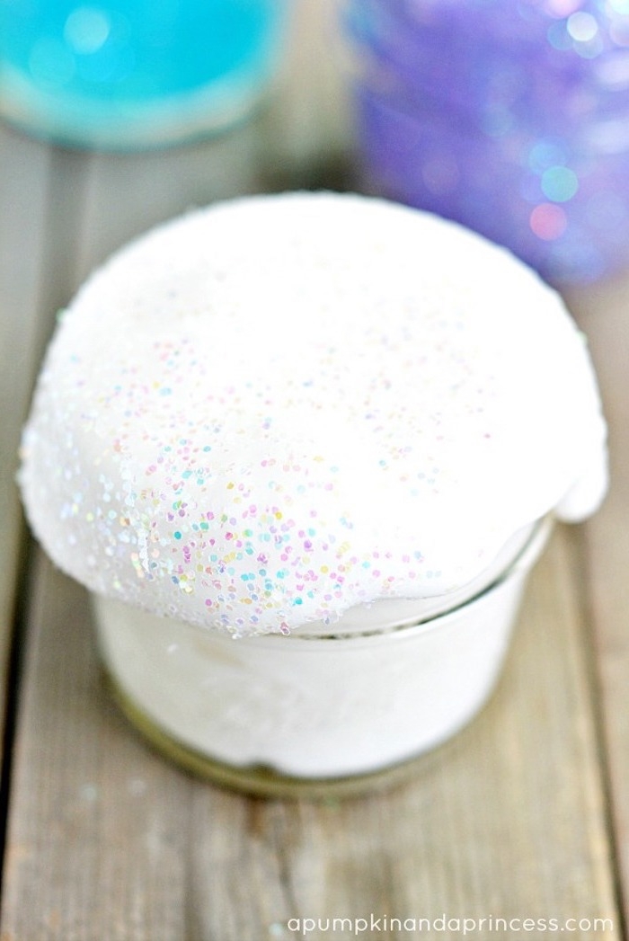snow-like white fluffy slime, decorated with iridescent glitter, shimmering in pink and blue, white and gold, overflowing from a small, clear glass pot