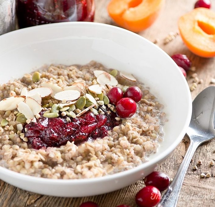 buckwheat mash inside a white ceramic bowl, topped with fresh cranberries and cranberry sauce, pumpkin seeds and almonds, healthy breakfast ideas, metal spoon nearby