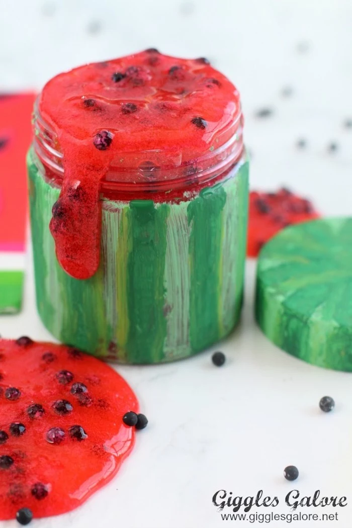 watermelon slime in red, with little black beads for the seeds, poured into a small glass jar, painted in green stripes, like a watermelon