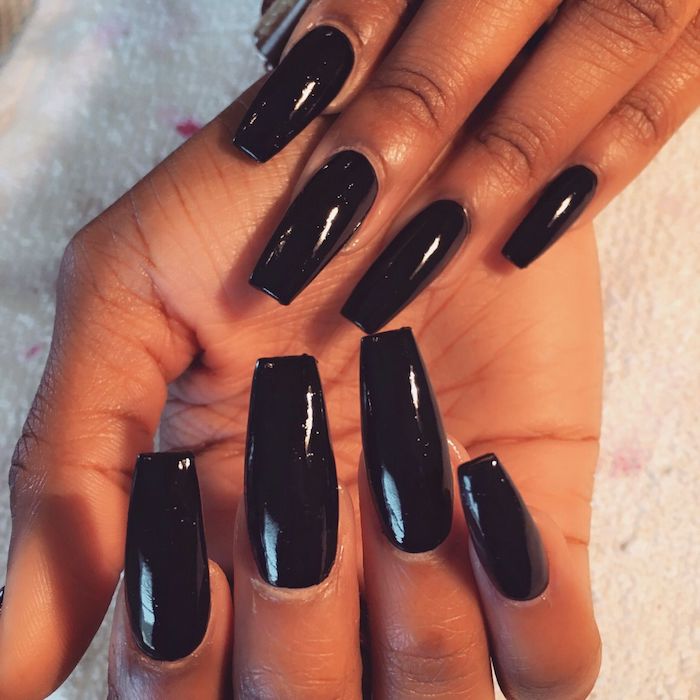 black smooth and glossy nail polish, on long squoval nails, attached to a pair of brown hands, resting on a towel-like fabric