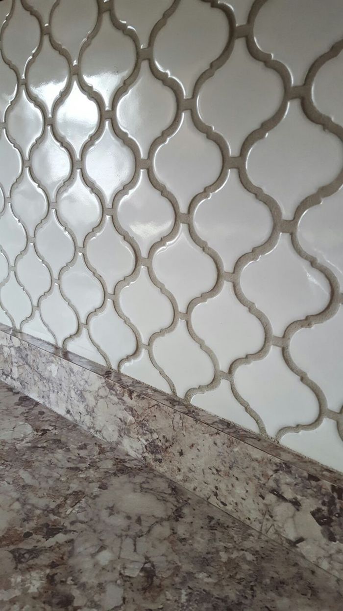 extreme close up of an arabesque tile backsplash, in milky white, with beige joints, near a spotty beige, smooth counter top