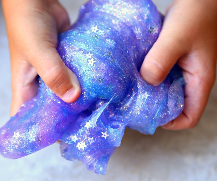 tiny toddler's hands, kneading a piece of galaxy-colored goop, how to make slime without borax, blue and purple colors, decorated with silver stars