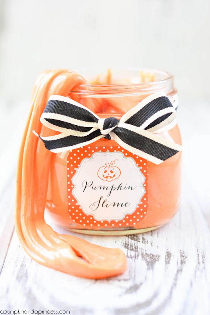 pumpkin slime in orange, inside a small clear jar, with orange and white label, and a black and white ribbon, tied in a bow, slime recipe without borax, light wooden surface
