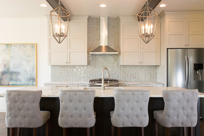 candle-shaped lights, inside two metal lanterns, hanging from the ceiling of a kitchen, marble counter top, pale grey herringbone backsplash 