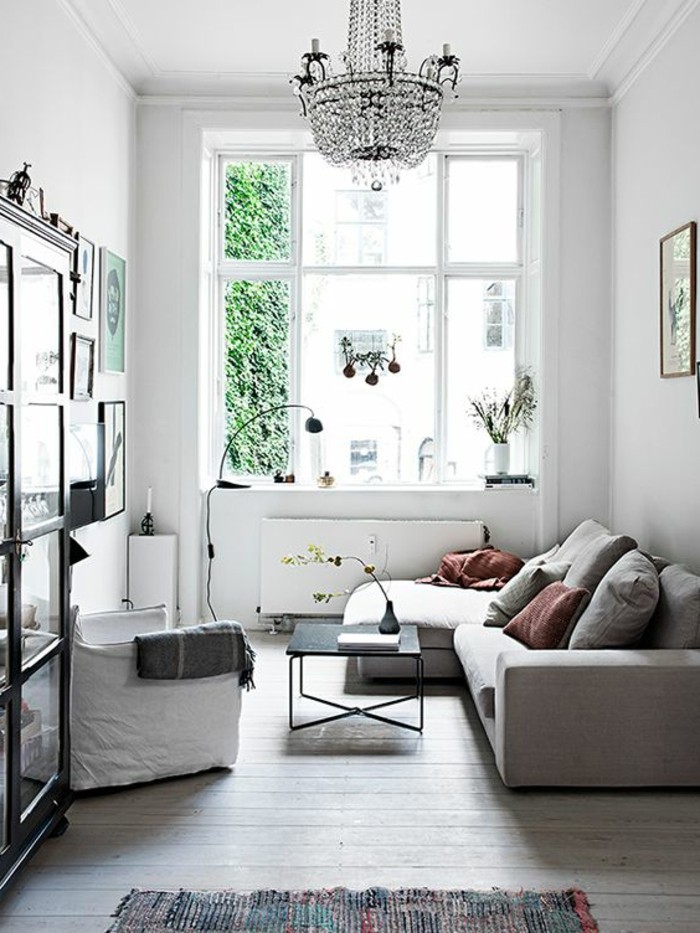 crystal chandelier inside a white room, with a large window, and a pale beige corner sofa, simple living room designs, black coffee table, and a white armchair 