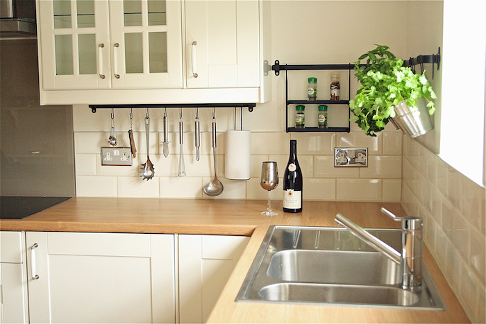 counter tops made from wood, in a light color, with an inbuilt metal sink, and white cabinets, white subway tile pattern on the walls