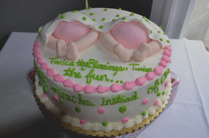 neon green and pale pink frosting, on a white cake, decorated with two sets of baby legs, in pink nappies, under a white blanket with green polka dots