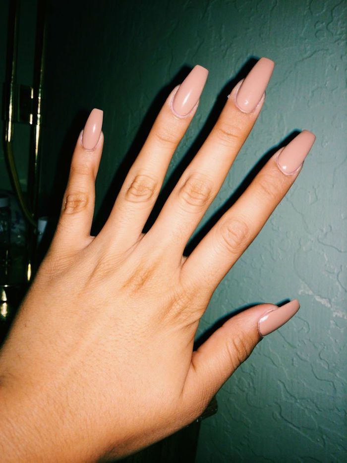 thin and long fingers, on a hand with long, coffin-style nails, painted in a glossy, nude pinky beige nail polish, dark grey background