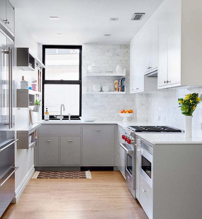 laminate floor in a small kitchen, with pale grey and white cabinets, light marble subway tile kitchen backsplash, and a slide up window