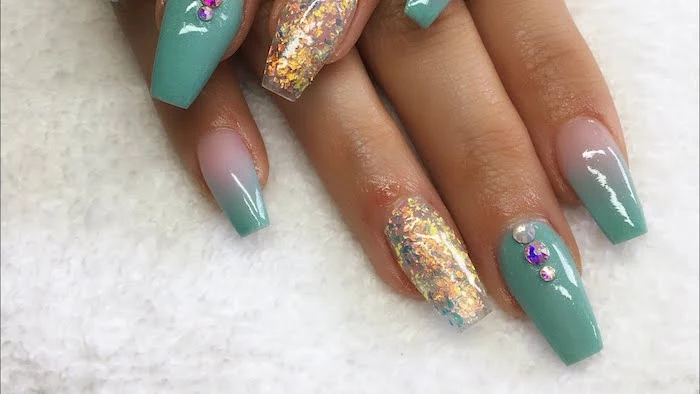 turquoise coffin acrylic nails, decorated with pale pink, gold and blue glitter, and rhinestones in white, purple and iridescent silver