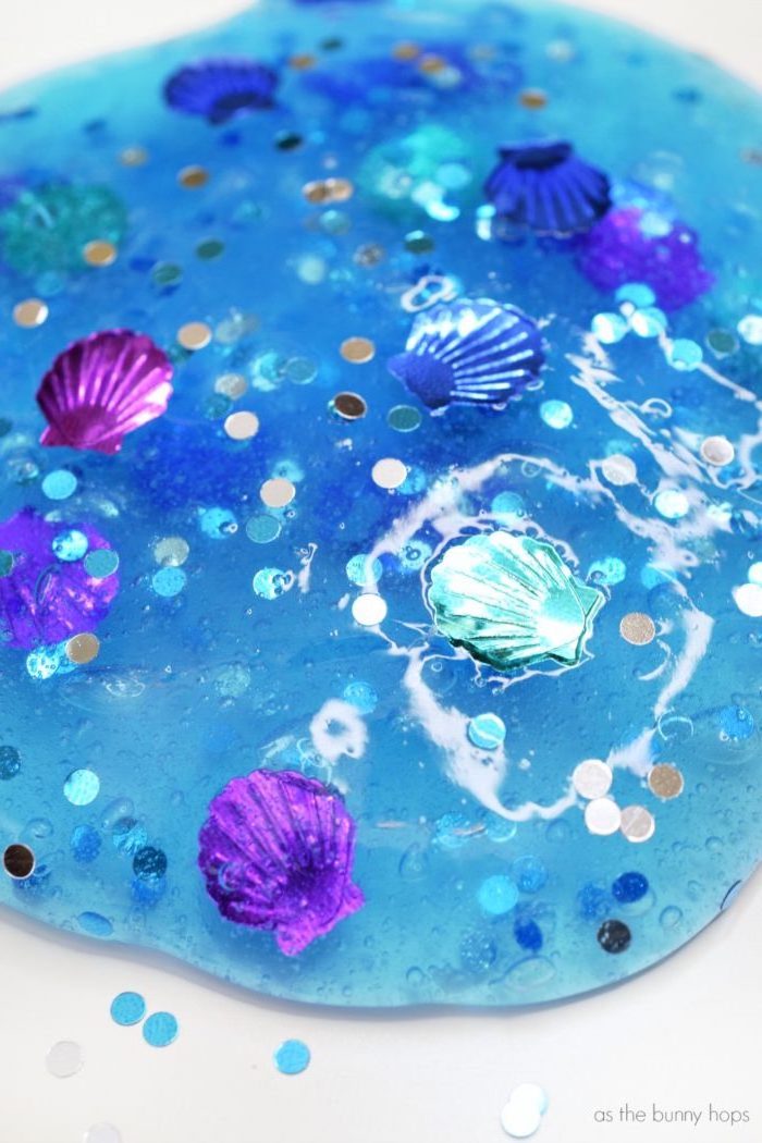water-like blue goo, decorated with glitter flakes in silver, light and dark blue, slime recipe without borax, with little plastic shell-decorations, in different colors