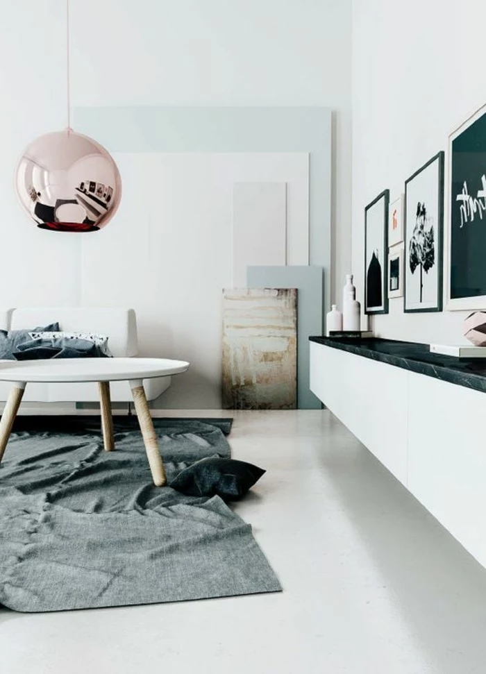 room setup ideas, round metallic lamp in pink, hanging above a white coffee table, inside a white room, with grey rug, and several framed artworks