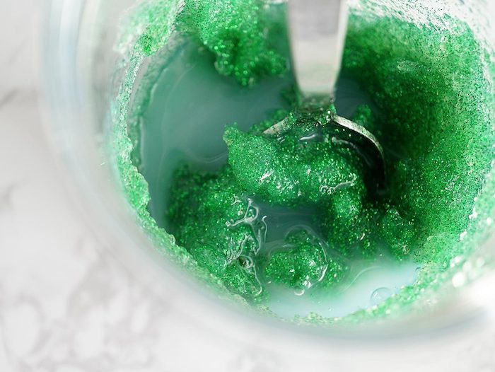 slushy green compound, with milky liquid, and slimy lumps, how to make slime without borax, inside a glass container, with a metal spoon